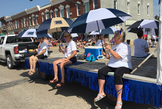 people sittiing on a parade float with blue and white umbrellas